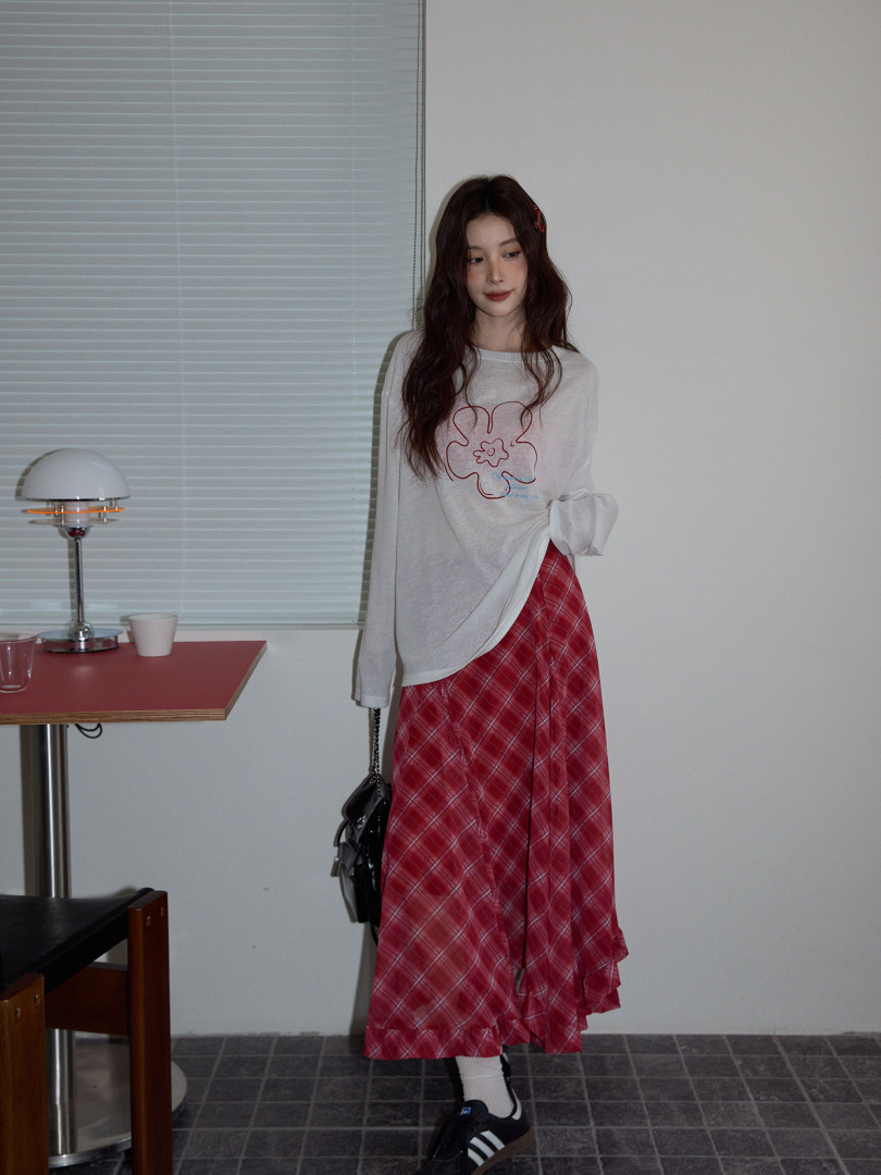 Model wearing a white long-sleeve top with a red plaid skirt and black shoes