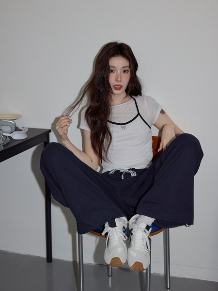 Model wearing a white layered top with navy wide-leg pants and white sneakers