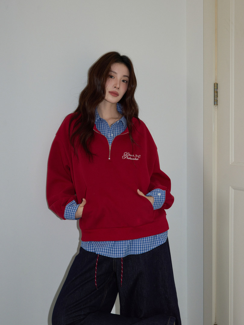 Model wearing a red quarter-zip pullover layered over a blue check shirt with wide-leg black pants