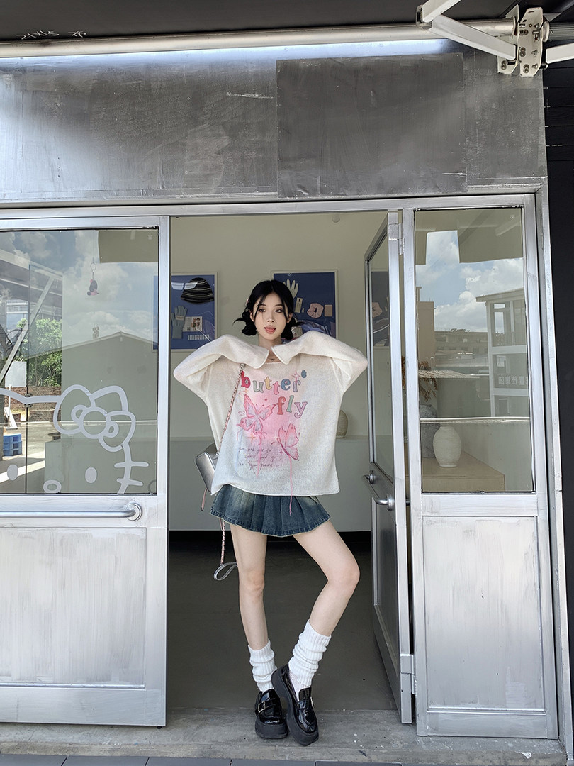 Woman wearing a white butterfly graphic sweater with a denim mini skirt, socks, and black shoes