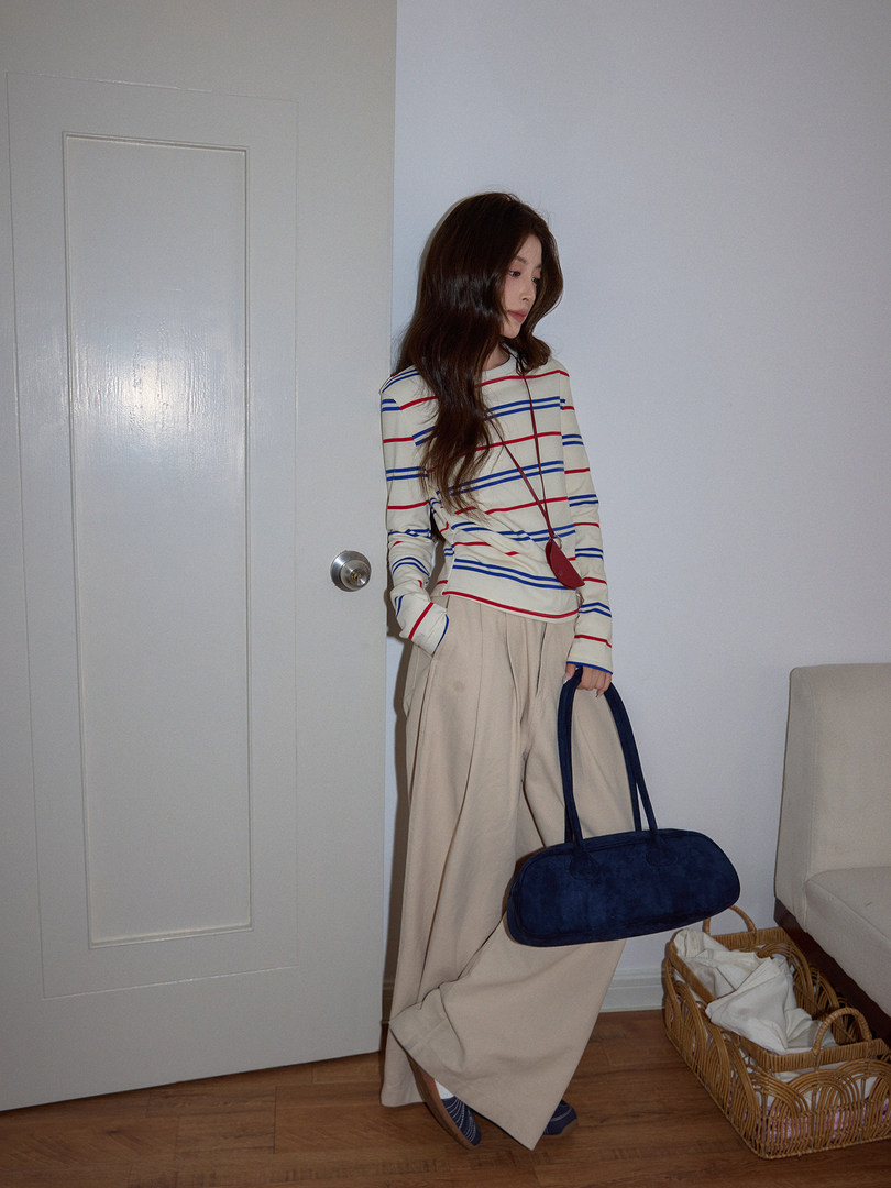 Model wearing a striped long-sleeve top with wide-leg beige pants and a navy shoulder bag
