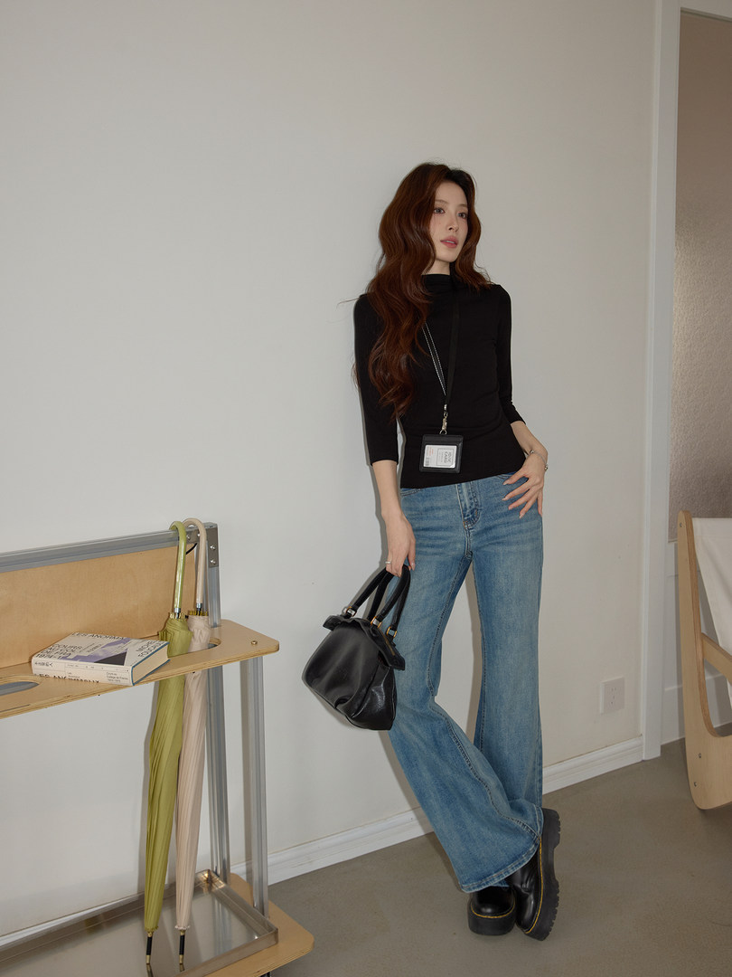 Model wearing a black top with wide-leg jeans and carrying a black handbag