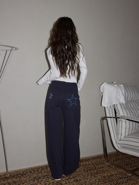 Model wearing navy wide-leg pants with star graphics and a white long-sleeve top