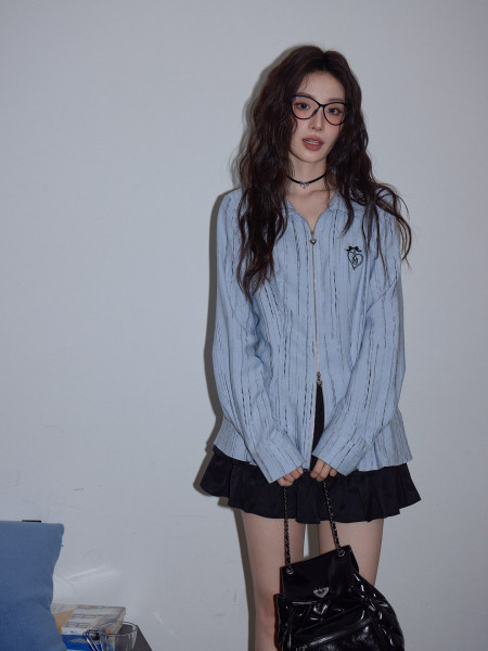 Model wearing a light blue zip-up top with a black mini skirt and black handbag