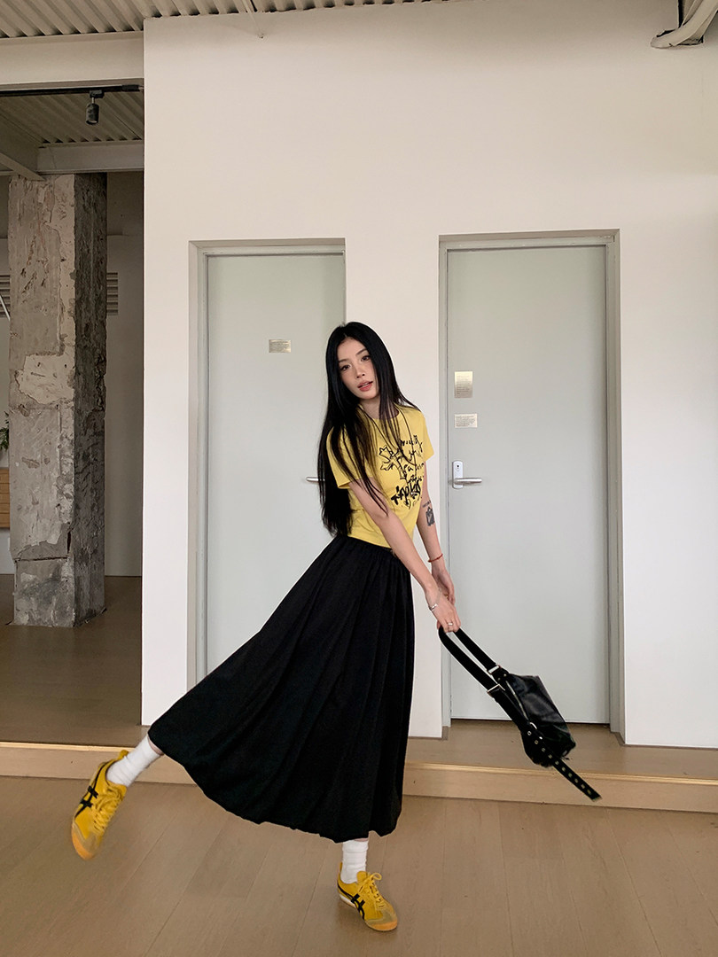 Model wearing a yellow graphic T-shirt with a long black skirt and yellow sneakers