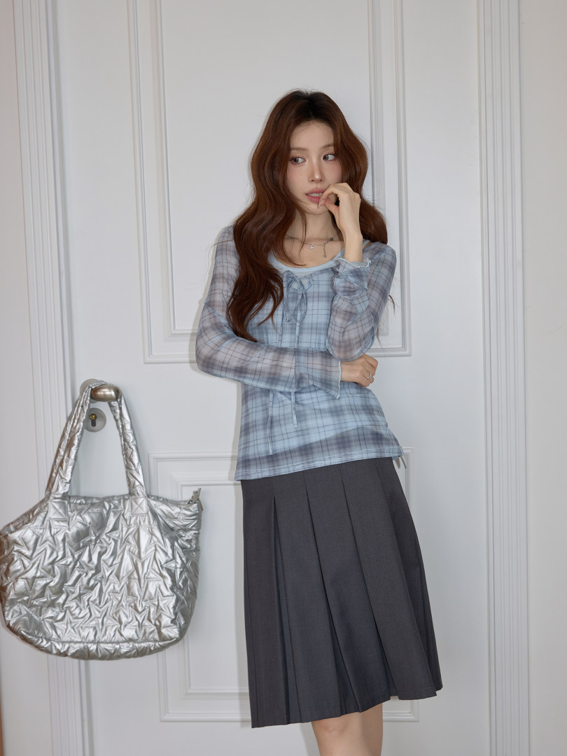Woman modeling a light blue plaid top with a black pleated skirt and silver tote bag