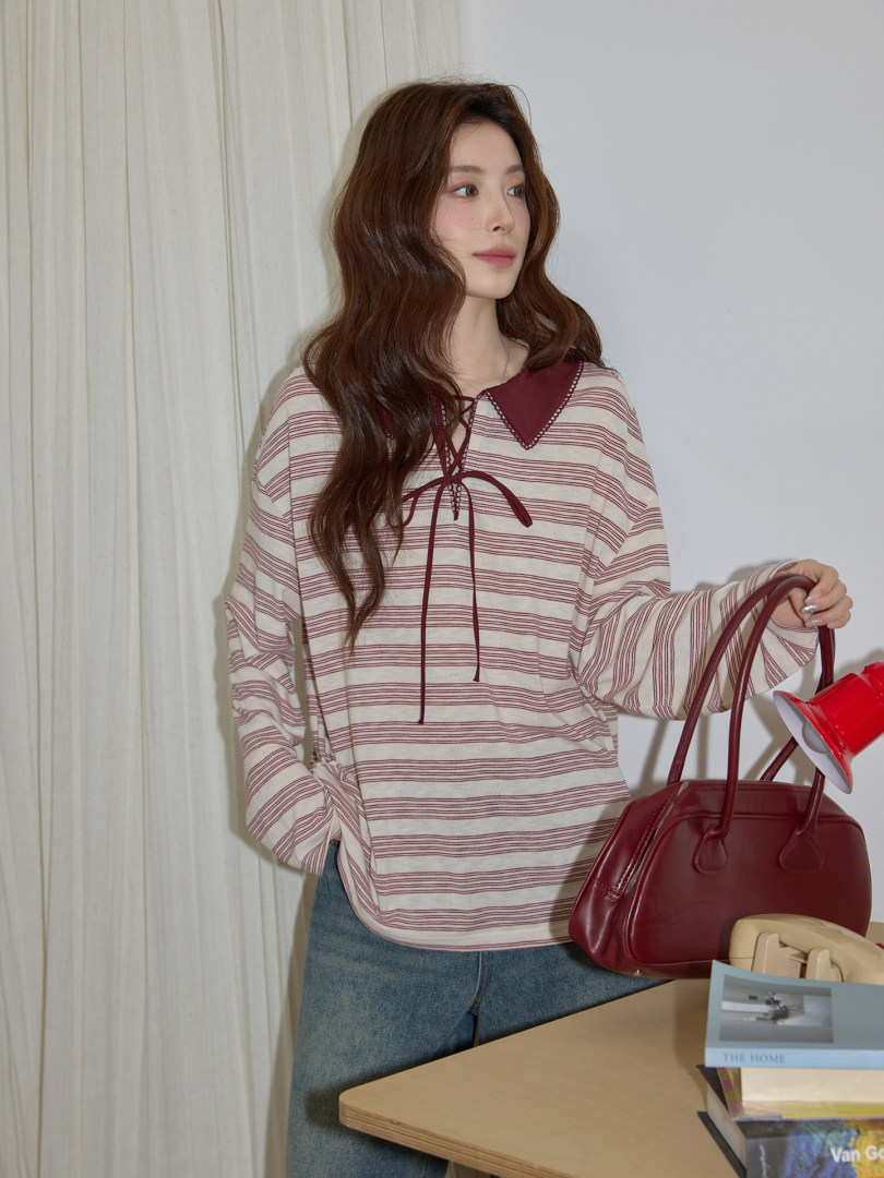 Model wearing a striped long-sleeve top and carrying a burgundy handbag