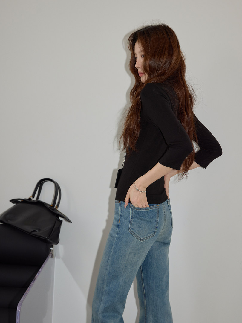 Model wearing a black fitted top with light blue jeans beside a black handbag