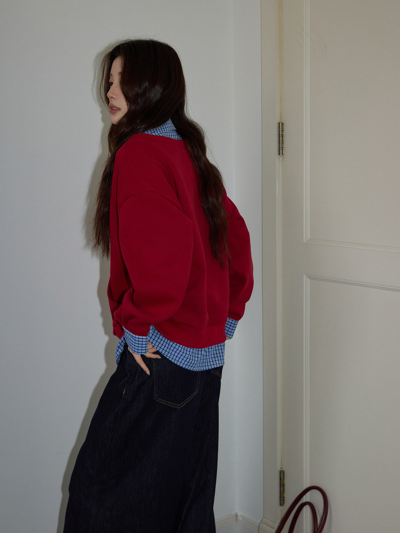 Model wearing a red oversized sweater layered over a blue check shirt with dark jeans