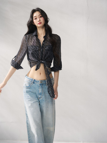 Model wearing a sheer black tie-front blouse with light-wash jeans