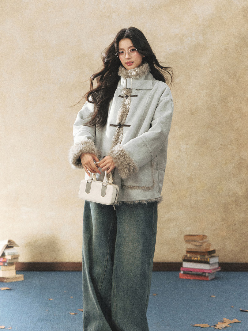 Model wearing a light gray fur-trimmed winter coat and holding a small handbag
