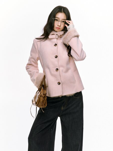 Model wearing a light pink fur-trimmed coat with dark jeans and a small brown handbag