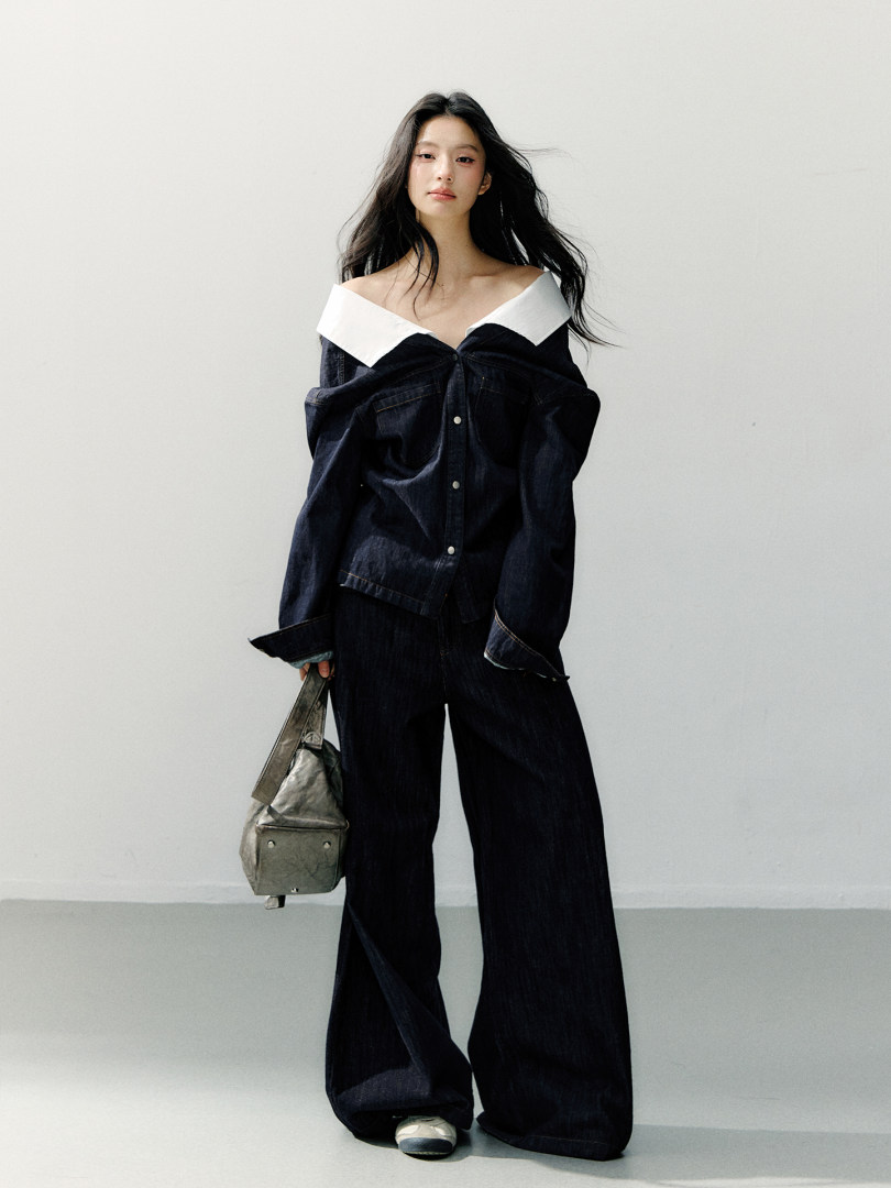 Model wearing a dark denim off-shoulder jacket and wide-leg pants with a metallic handbag