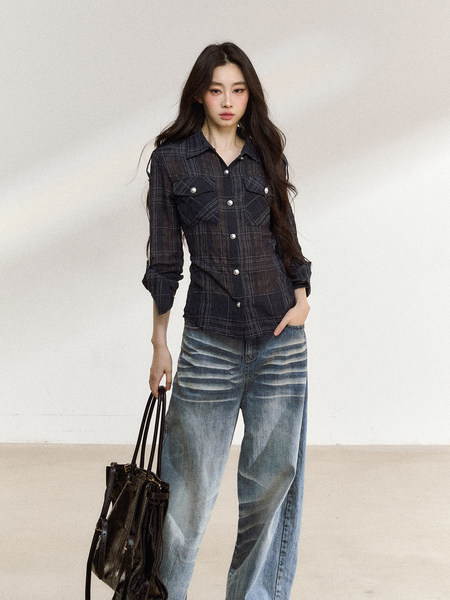 Model wearing a dark plaid button-up shirt with faded wide-leg jeans and a black tote bag.