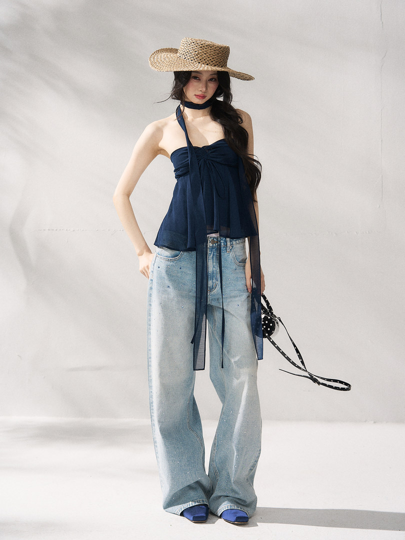 Model wearing a navy halter top with wide-leg jeans and a straw hat