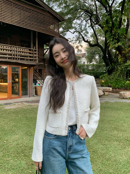 Woman wearing a white textured cardigan with pearl trim and blue jeans outdoors