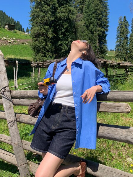 Woman wearing a blue button-up shirt with a white tank top and dark denim shorts outdoors