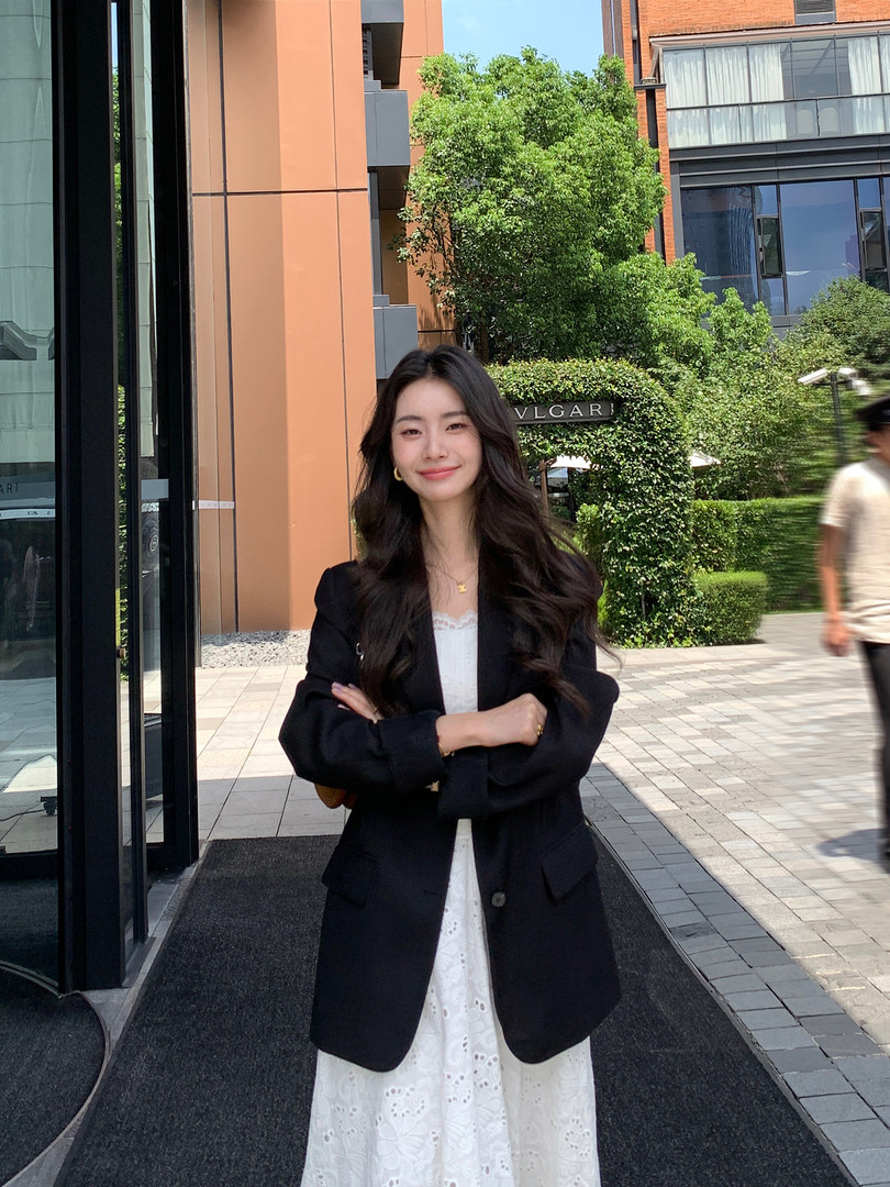 Woman wearing a black blazer over a white dress outdoors
