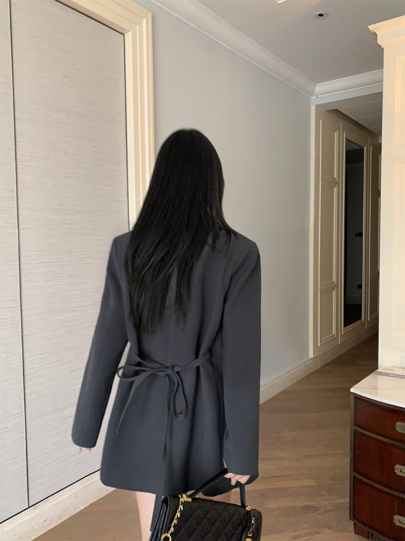 Model wearing a dark belted blazer-style coat indoors
