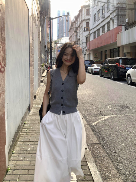 Woman wearing a gray sleeveless button vest with a white skirt on a city street