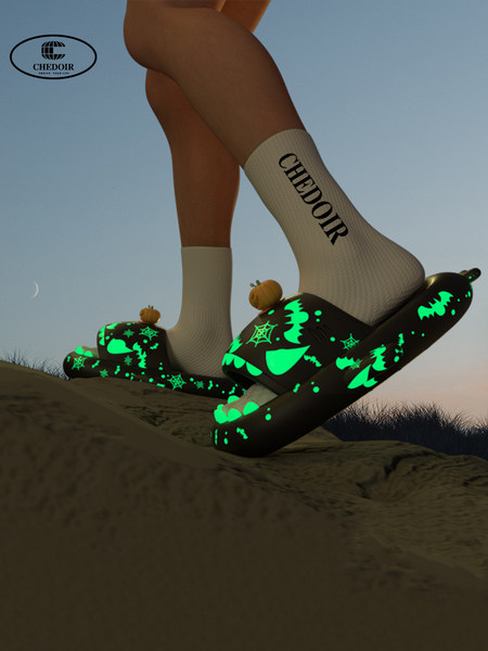 Model wearing black glow-in-the-dark Halloween-themed slippers with green graphics
