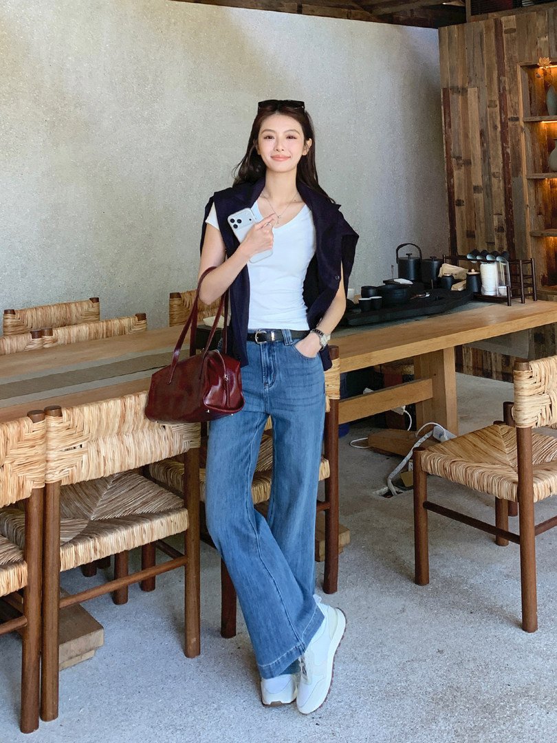 Woman wearing a casual outfit with white top, blue jeans, navy vest, and burgundy handbag