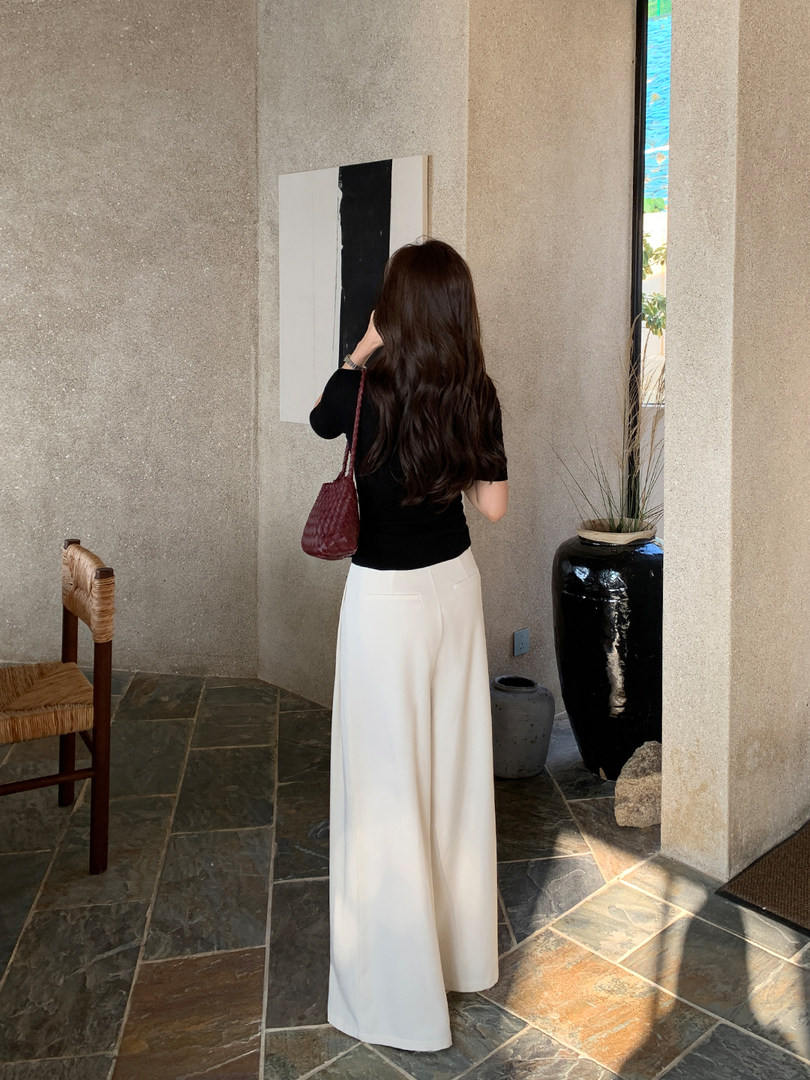 Woman wearing a black top and white wide-leg pants indoors