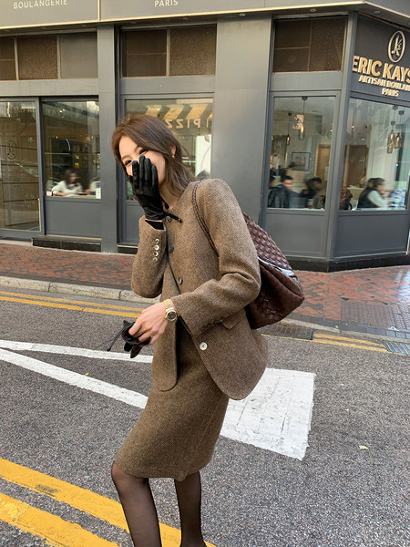 Woman wearing a brown textured blazer and matching skirt with gloves and a woven bag