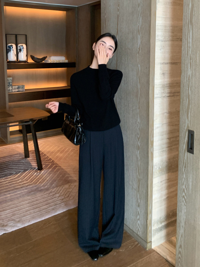 Woman wearing a black long-sleeve top with wide-leg pants and a black handbag