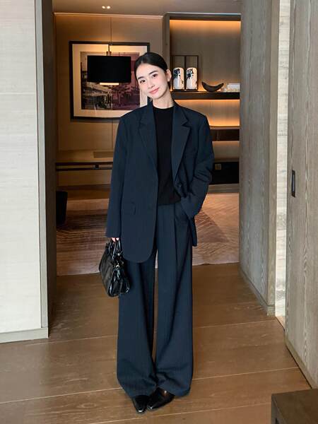 Woman wearing a dark navy oversized suit with wide-leg trousers and a black top, holding a black handbag