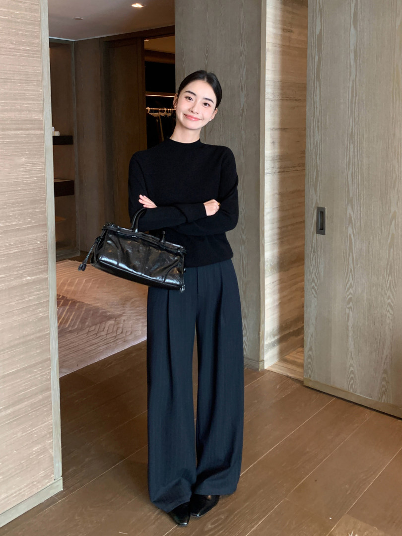 Model wearing a black long-sleeve top with wide-leg navy pants and a black handbag