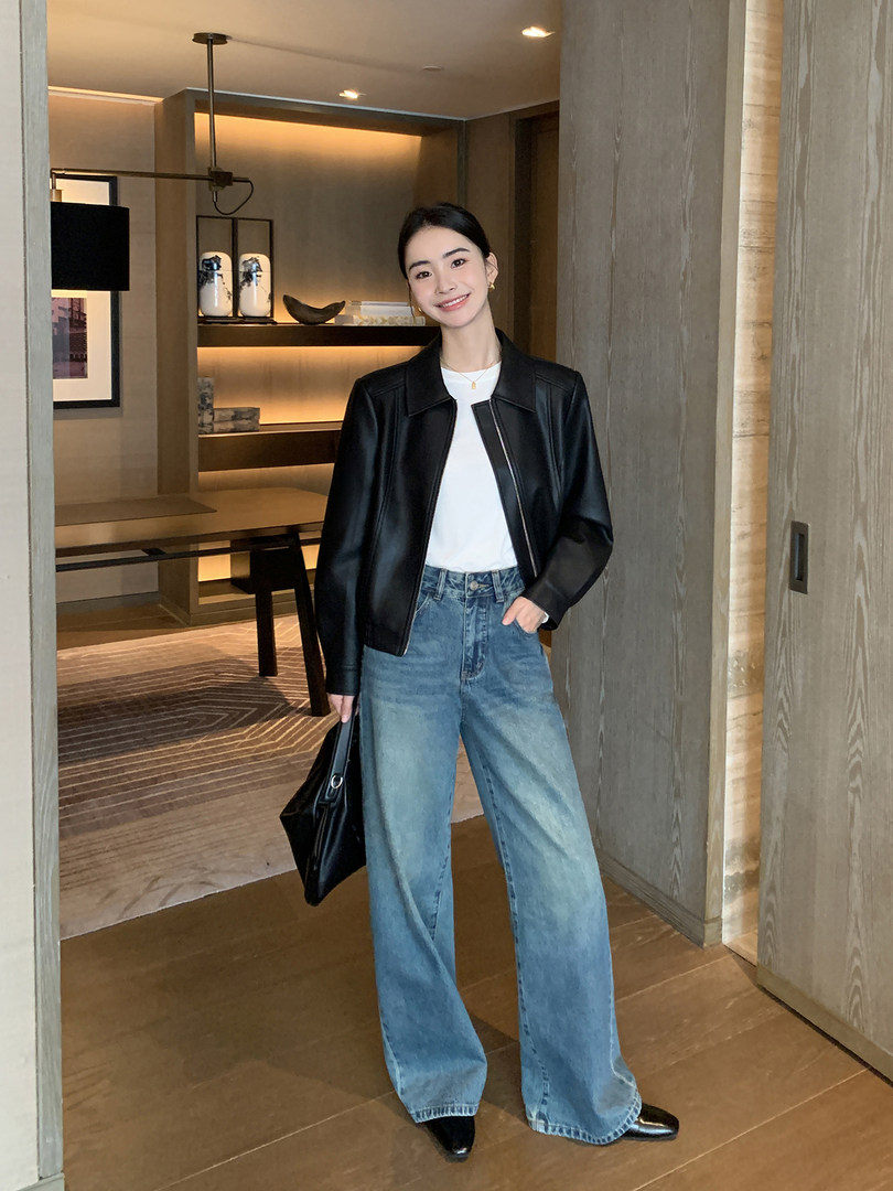 Woman wearing a black jacket with white top and wide-leg blue jeans, holding a black bag