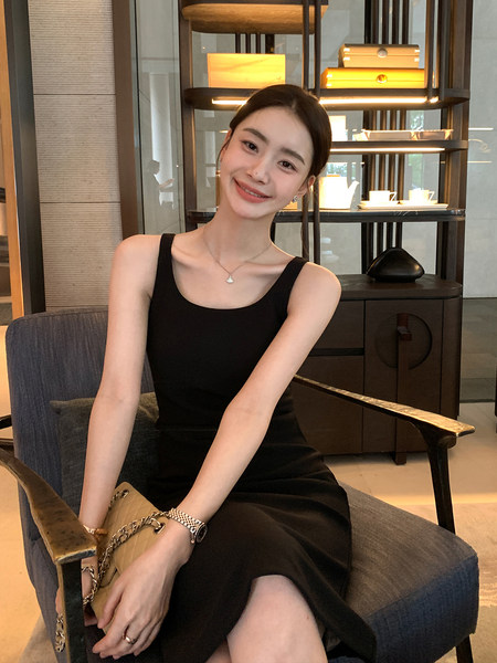 Woman wearing a black sleeveless dress seated indoors