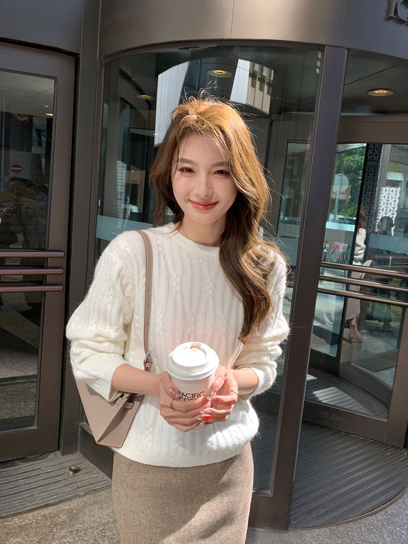 Woman wearing a white knit sweater and beige skirt while holding a coffee cup