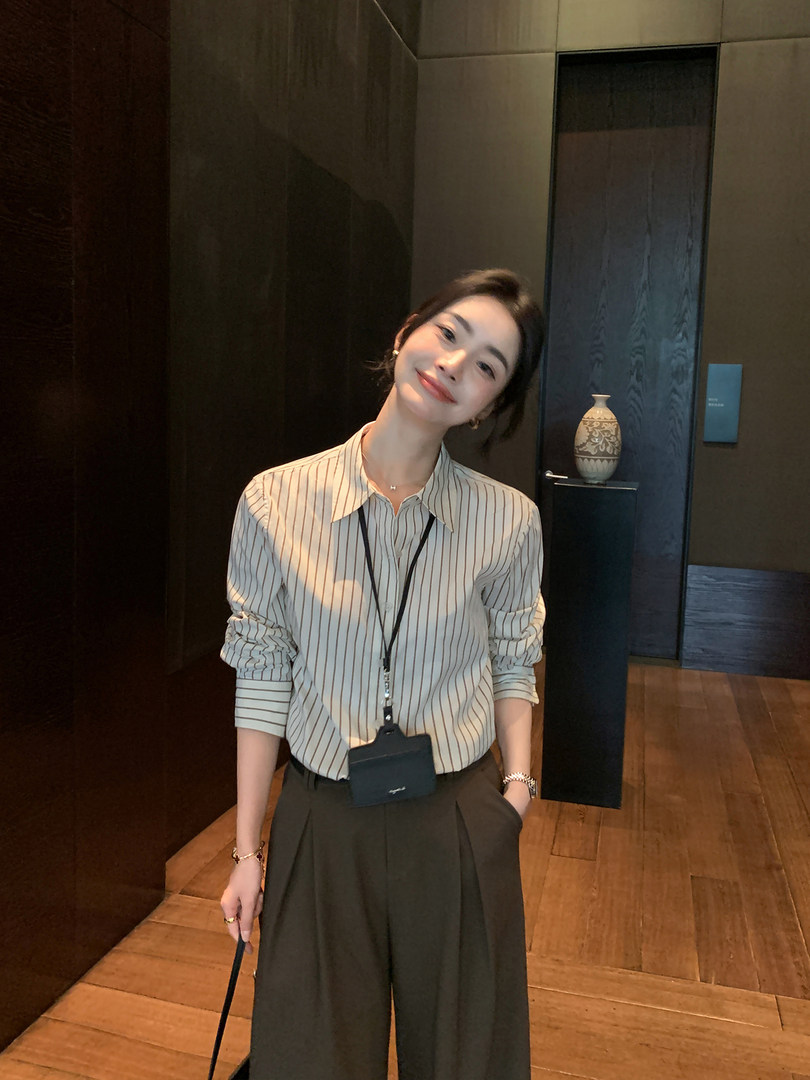 Woman wearing a striped button-up shirt with wide-leg trousers in a polished indoor outfit