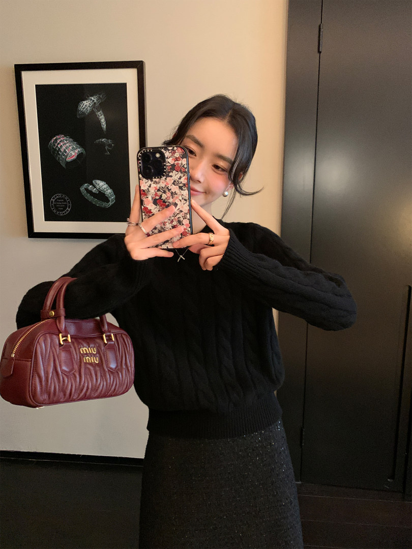 Mirror selfie of a woman wearing a black knit sweater and holding a burgundy Miu Miu handbag