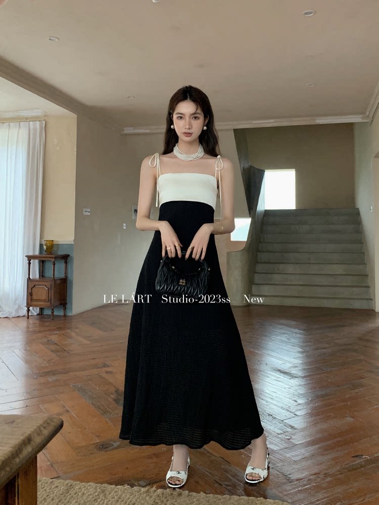Model wearing a black and white sleeveless maxi dress holding a small handbag