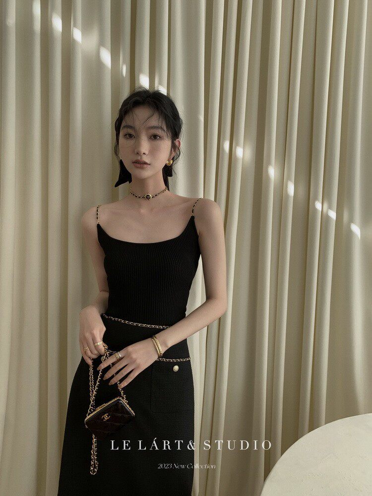 Model wearing a black fitted sleeveless dress with chain accessories