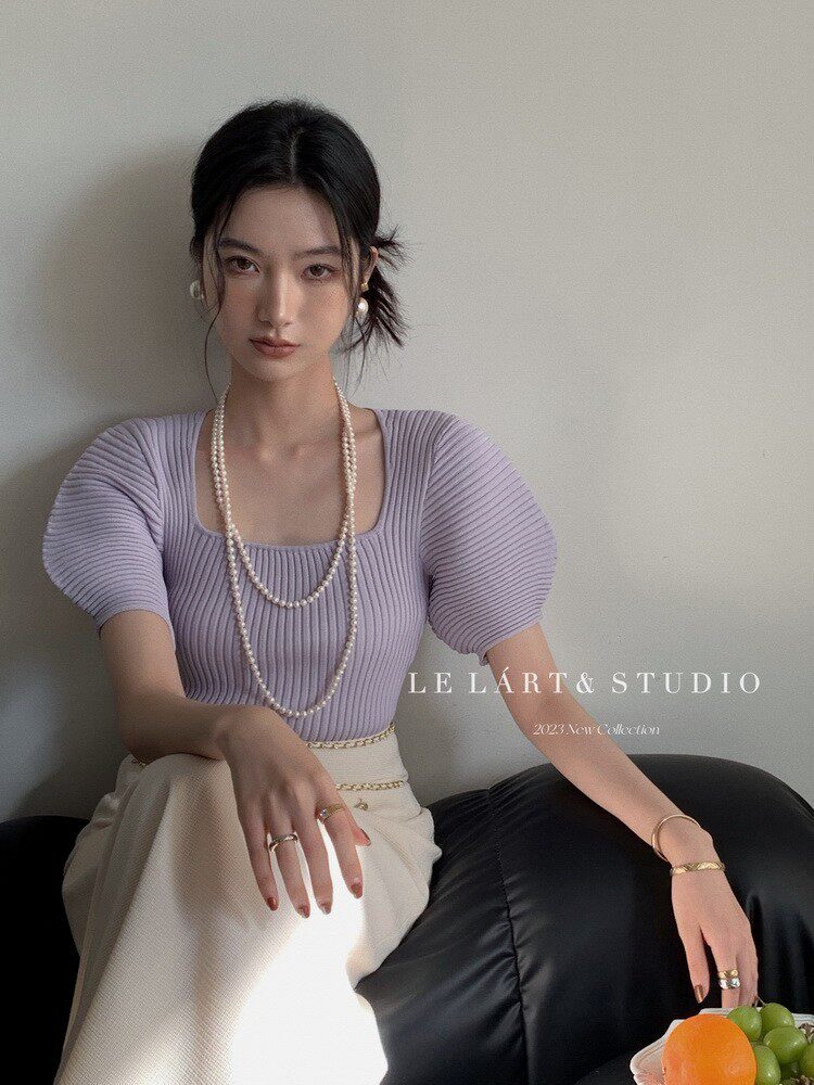 Woman wearing a lavender ribbed puff-sleeve knit top with layered pearl necklaces