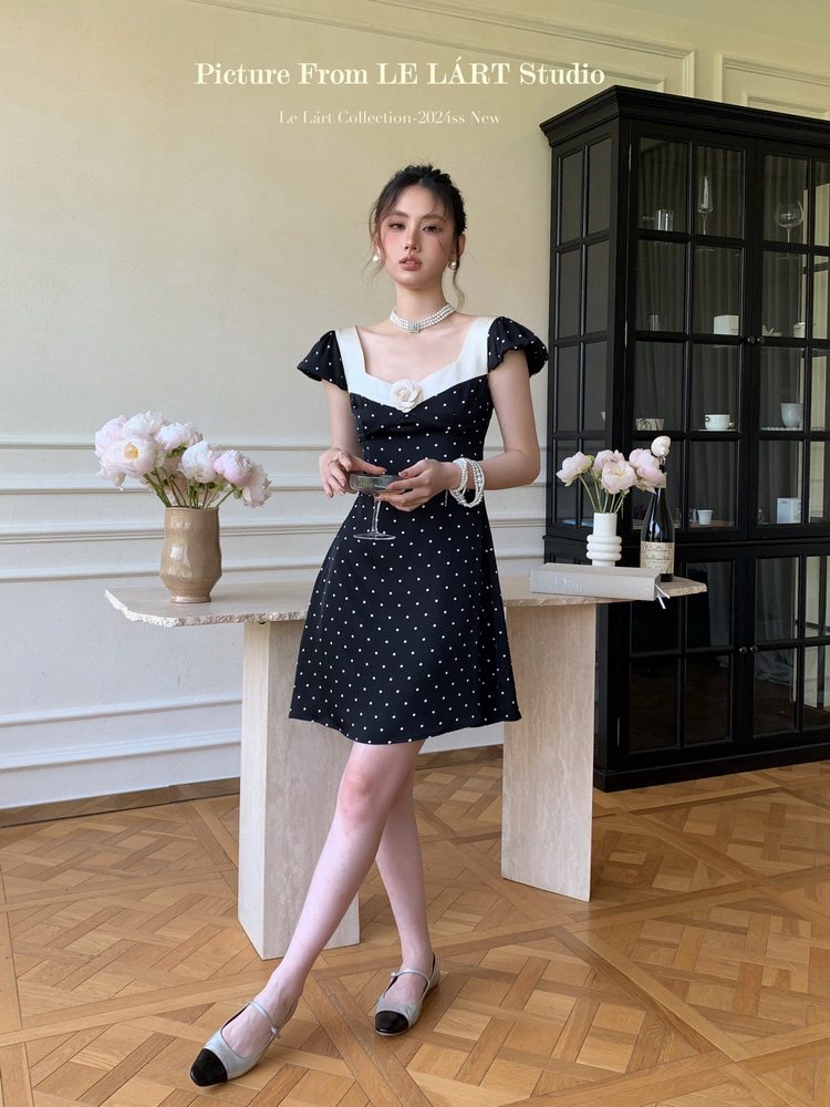 Woman wearing a black polka dot short dress with white trim in a styled indoor setting