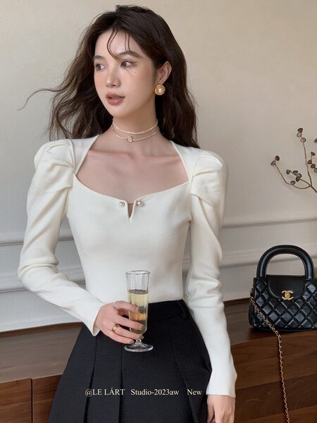 Woman wearing a white long-sleeve fitted top with a square neckline and black skirt