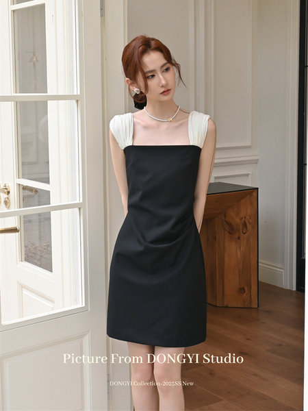 Model wearing a black mini dress with white shoulder straps in a studio setting