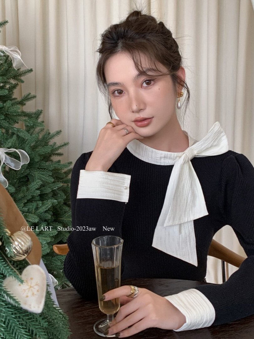 Black ribbed top with white bow collar and matching cuffs worn by a model