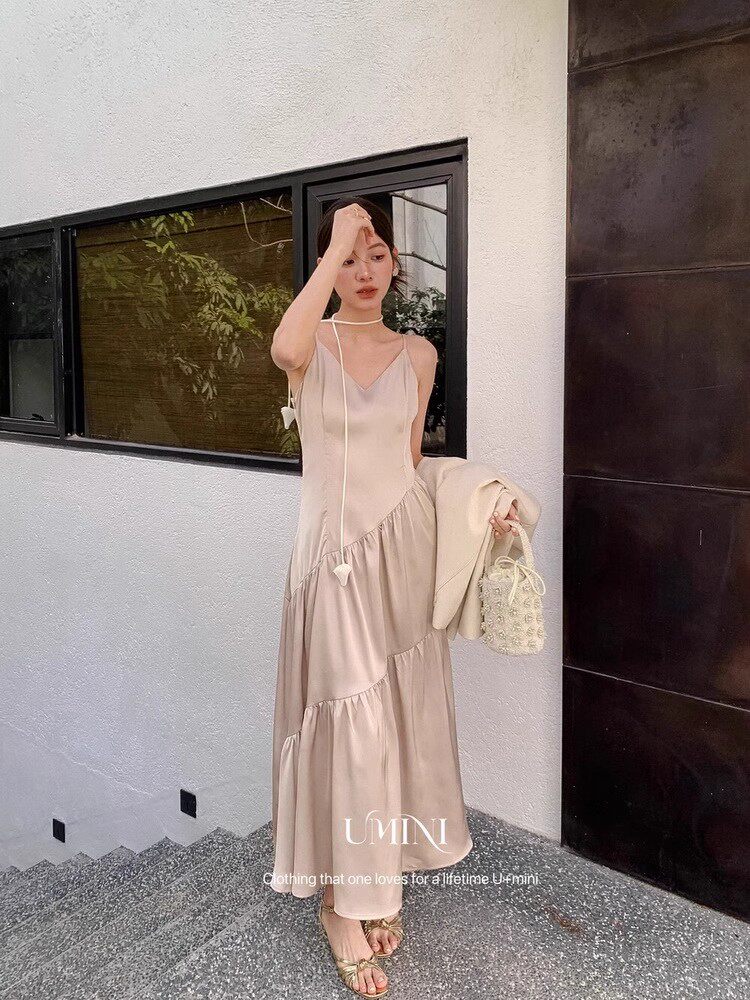 Woman wearing a light beige sleeveless maxi dress and holding a small handbag
