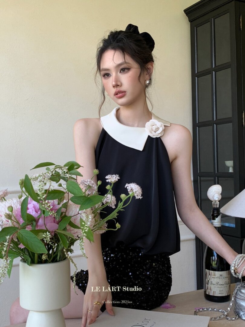 Model wearing a black sleeveless top with white collar and flower detail paired with a black sequined skirt