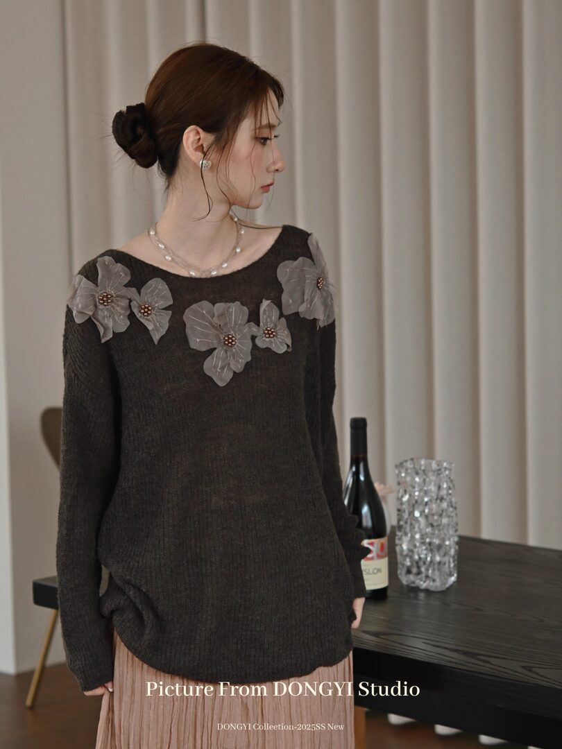 Woman wearing a dark knit sweater with floral appliques and a sheer layered look