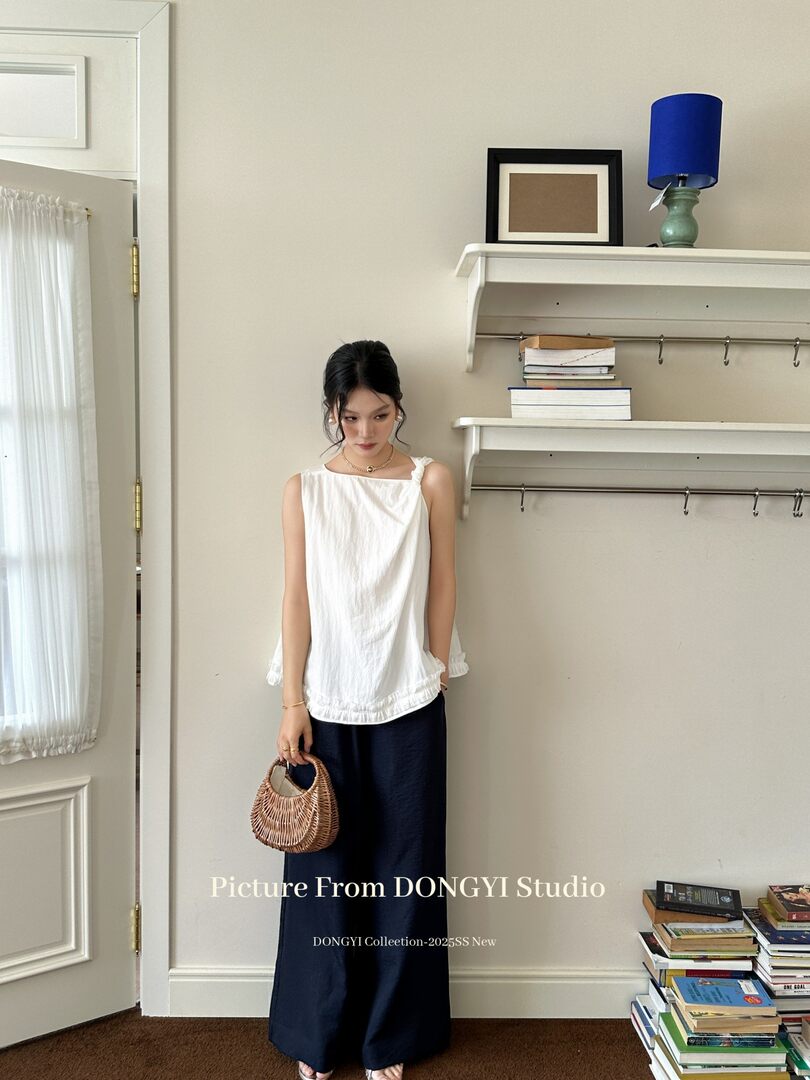Model wearing a white sleeveless top with navy wide-leg pants and a woven handbag