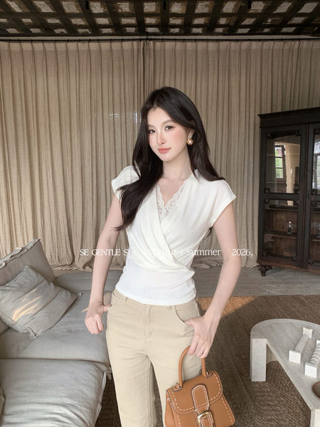 Woman wearing a white wrap-style top and beige pants, holding a brown handbag
