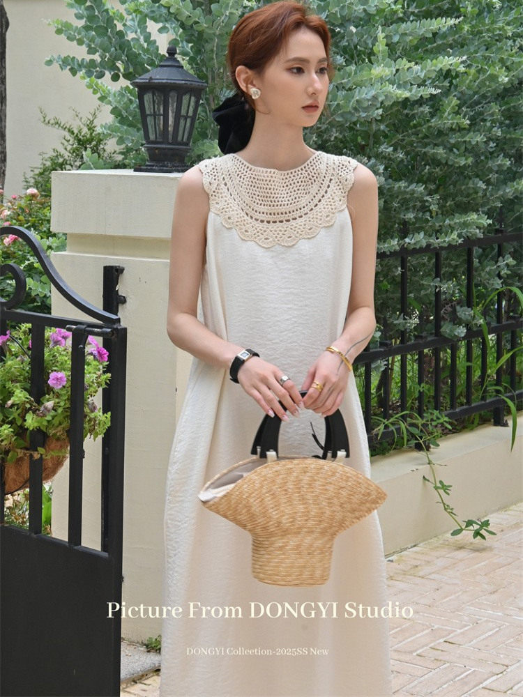 Model wearing a white sleeveless maxi dress with a crochet neckline, holding a woven straw handbag