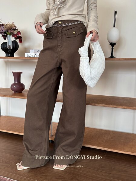 Model wearing brown wide-leg pants with a beige top and white woven handbag